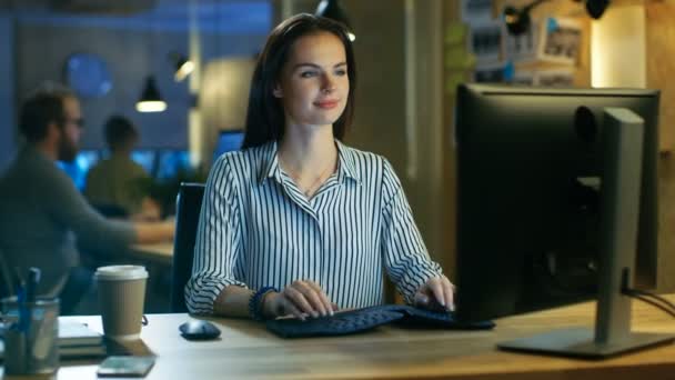 Gyönyörű fiatal nő működik a személyi számítógép, bájosan mosolyog a kamera. Ő dolgozik egy Modern tetőtéri stúdió irodaterület. — Stock videók