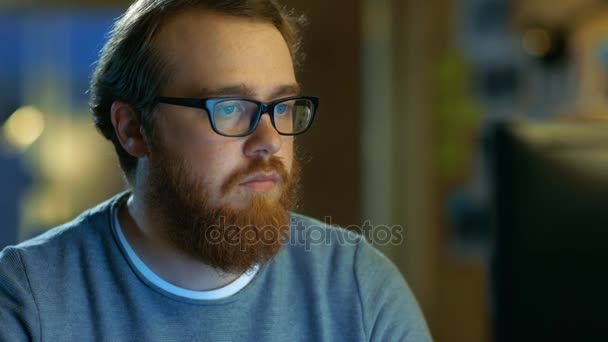 Jeune homme créatif barbu avec des lunettes pense à un problème tout en travaillant sur son ordinateur personnel . — Video