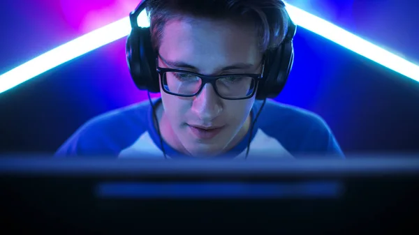 Professional Gamer Plays in MMORPG/ Strategy/ Shooter Video Game on His Computer. He's Participating in Online Cyber Games Tournament, Plays at Home, or in Internet Cafe. He Wears Glasses and Gaming Headphones, Talks into Microphone. — Stock Photo, Image