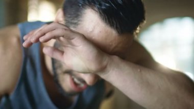 Yakın çekim Shot yorgun Bend kaslı adamın alnına bir elle mendil ve kamera ve dinlenirken yoğun çalışmadan sonra görünüyor. Bir spor salonunda o ve ter içinde kaplı. O bir nefes yakalamak için çalışır.