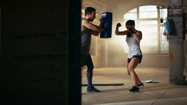 Mujer atlética golpea saco de boxeo que su pareja / entrenador sostiene. Ella es luchadora profesional y está entrenando en un gimnasio . — Vídeo de stock