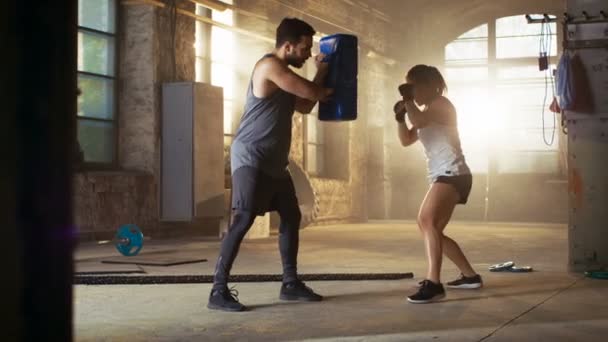 Mujer atlética golpea saco de boxeo que su pareja / entrenador sostiene. Ella es luchadora profesional y está entrenando en un gimnasio . — Vídeos de Stock
