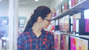 Güzel ve genç birbayan elektronik mağazasında 4 k en son modelleri ile raflar tarama Uhd TV yürür. O büyük, parlak Modern mağaza yeni aygıt olmadığı gülümsüyor.