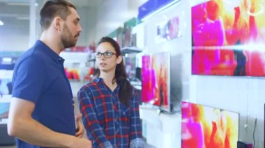 Elektronik mağazasında profesyonel danışman Uhd Tv satın almak için yeni bir 4 k için benzeyen genç bir kadın için uzman önerileri sağlar. Bu parlak, Modern saklamak tüm en son Tv modelleri asılı duvarda.