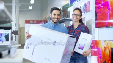 Elektronik mağaza mutlu genç pozlar yeni satın aldığınız casus uçak ve Tablet bilgisayar ile çift. Mağaza büyük ve parlak, tüm en son TV, kamera ve akıllı telefonlar vardır.