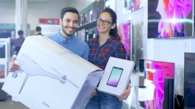 Elektronik mağazasında yeni satın aldığınız casus uçak ve Tablet bilgisayar ile pozlar mutlu genç çift. Mağaza büyük ve parlak, tüm en son TV, kamera ve akıllı telefonlar vardır.