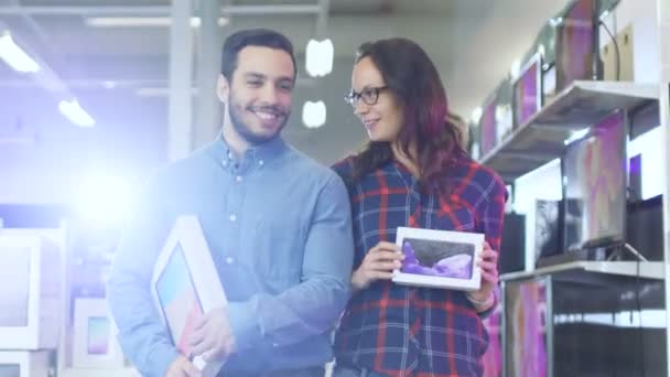 幸せなカップルは、電器店を歩いて、彼らは彼女のための新しいスマート フォン タブレット コンピューターの最新モデルを購入しました。ショッピング センターは大きな、明るい、最新エレクトロニクスの完全. — ストック動画