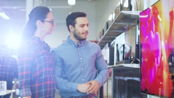 Jovem casal Compras para uma nova televisão 4K UHD Set na loja de eletrônicos. Estão a decidir o melhor modelo para a sua feliz casa de família. . — Vídeo de Stock