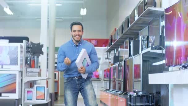 Dans le magasin d'électronique, Young Man détient une tablette d'ordinateur nouvellement achetée et saute heureusement avec elle. Tourné au ralenti. Store est moderne, lumineux et dispose de tous les derniers appareils . — Video