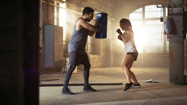 Atlética mujer golpea saco de boxeo que su pareja / entrenador sostiene — Foto de Stock