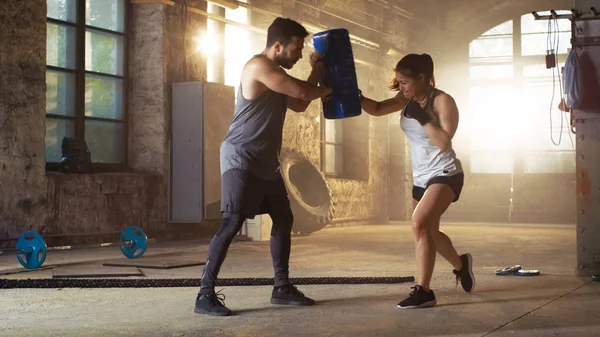 Спортивная женщина бьет боксерскую сумку, которую держит ее партнер / тренер — стоковое фото