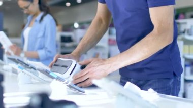 Elektronik mağaza genç adam çalışır içinde sanal gerçeklik kulaklıktaki, görüntüleri ve hemen istiyor satın bir tarafından bu hayrete. Modern, en son aygıt olmadığı Bright mağaza o.