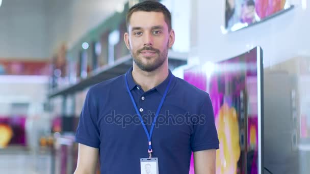 Retrato de um consultor especialista profissional sorri e olha para a câmera como fica no brilhante, loja de eletrônicos moderna cheia de modelos mais recentes de televisores, câmeras, tablets e outros dispositivos. . — Vídeo de Stock