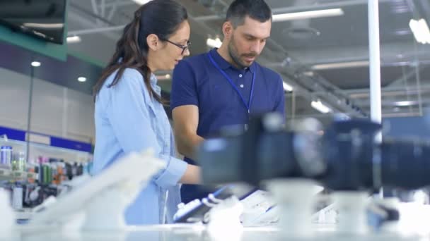 Dans l'Electronics Store Consultant donne des conseils professionnels à une jeune femme, elle envisage d'acheter une nouvelle tablette et a besoin de l'avis d'experts. Store est moderne, lumineux et a tous les nouveaux appareils . — Video