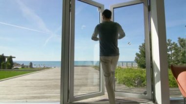 Balkonlu ve Deniz Manzaralı Teras üzerine yürüyen bir genç adam açılış kapıları kadeh takip. Sun Shining ve mutlu adamdır. 