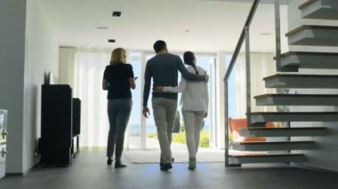 Profesyonel emlakçı gösterir şık Modern ev satın alma / yeni ev kiralamak için piyasada olan güzel genç bir çift için. Evin kat tavana uzanan pencereler ve sahil görünümü vardır.