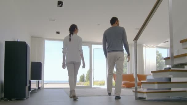 Молодая пара в недавно купленном доме смотрит на море через пол, чтобы открыть окна. Их роскошный дом яркий, современный со вкусом сделанный интерьер . — стоковое видео