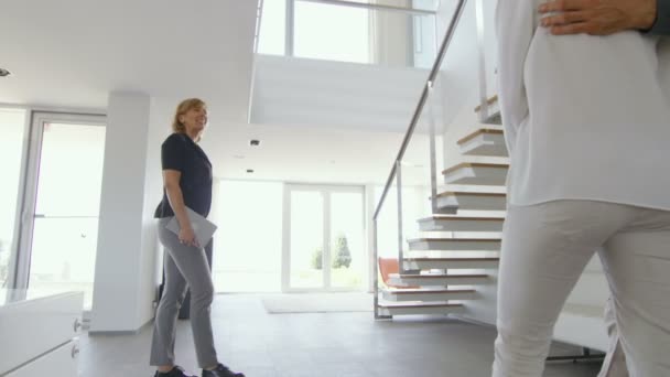 Professionell fastighetsmäklare välkomnar vackra unga par i rymliga och moderna hem. Med golv till tak fönster och havsutsikt. — Stockvideo