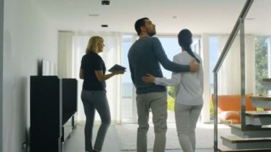 Profesyonel emlakçı gösterir şık Modern ev satın alma / yeni ev kiralamak için piyasada olan güzel genç bir çift için. Evin kat tavana uzanan pencereler ve sahil görünümü vardır.