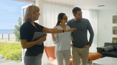 Profesyonel emlakçı gösterir şık Modern ev satın alma / yeni ev kiralamak için piyasada olan güzel genç bir çift için. Evin kat tavana uzanan pencereler ve sahil görünümü vardır.