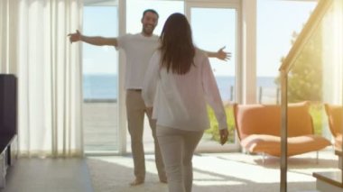 Güneşli oturma odasında, yakışıklı genç Spin-sarılmak onun güzel kız arkadaşı ve onlar kaldırdı. Onlar mutlu ve Sunny Deniz Manzaralı evim.