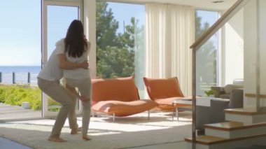 Güneşli oturma odasında, yakışıklı genç Spin-sarılmak onun güzel kız arkadaşı ve onlar kaldırdı. Onlar mutlu ve Sunny Deniz Manzaralı evim.