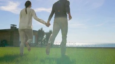 Güzel yaz günü mutlu çift bekle eller ve çıplak ayakla çimlerde çalıştırın. Güneşli onlardan önce mavi gökyüzü ve deniz görünümü.