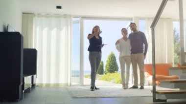 Emlakçı ile güzel bir genç çift için Tablet bilgisayar kontrollü akıllı ev gösterir. Evin kat tavana uzanan pencereler ve sahil görünümü vardır.