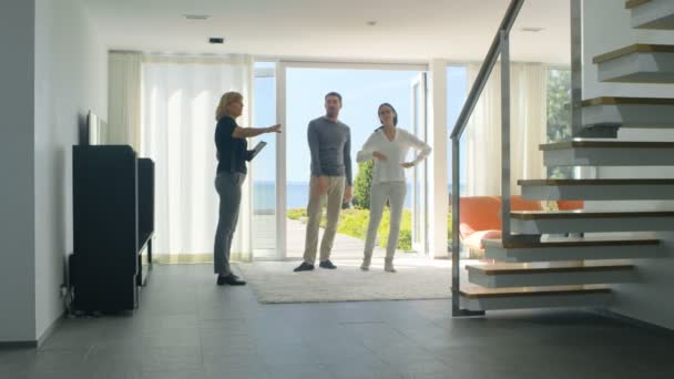 Professioneller Immobilienmakler zeigt stilvolles modernes Haus einem schönen jungen Paar, das auf dem Markt für Kauf / Vermietung eines neuen Eigenheims ist. Haus hat bodentiefe Fenster und Meerblick. — Stockvideo