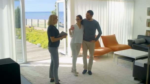 Profesionální realitní makléř ukazuje stylový moderní dům krásný mladý pár, kteří jsou na trhu pro nákup / pronájem nových domů. Dům má patro francouzskými okny a výhledem na moře. — Stock video