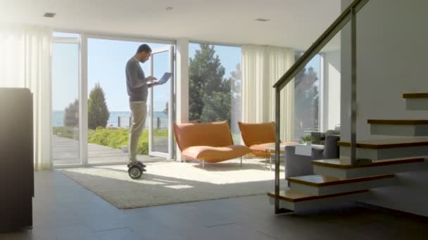 Indústria de tecnologia Empresário que trabalha a partir de casa usa computador portátil e passeios em torno da casa em seu Gyro Scooter. Sua casa moderna tem vista para o mar . — Vídeo de Stock