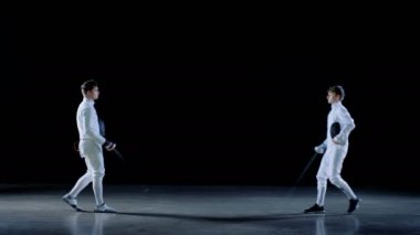 İki genç profesyonel eskrimcilerin selamlıyorum seyirci, maskeler ve başlangıç Kılıç dövüşü maç koymak. Siyah arka plan üzerine izole atış .