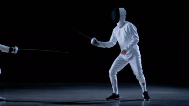 İki profesyonel eskrimcilerin göstermek ustaca kılıç onların folyo Fight. Onlar birden kenara çekilip kurtulmak, sıçrama ve itme ve saldır. Siyah arka plan üzerine ve yavaş hareket izole atış.