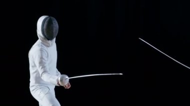 İki profesyonel tam donanımlı eskrimcilerin ustalıkla folyo ile mücadele. Lunges ve kazanır, o zafer kazanan maskesini alır. Atış yavaş hareket ve siyah arka plan izole. 