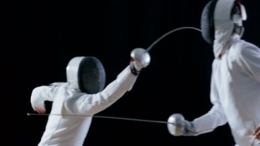 İki profesyonel tam donanımlı eskrimcilerin ustalıkla folyo ile mücadele. Bir Lunges ve WINS, o alır, onun maskesi tüm ihtişamıyla. Atış yavaş hareket ve siyah arka plan izole. 