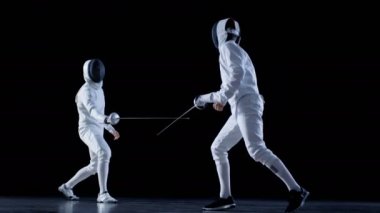 İki profesyonel tam donanımlı eskrimcilerin ustalıkla folyo ile mücadele. Onlar saldırı, savunma, sıçrama, itme ve saldır. Atış yavaş hareket ve siyah arka plan izole. 