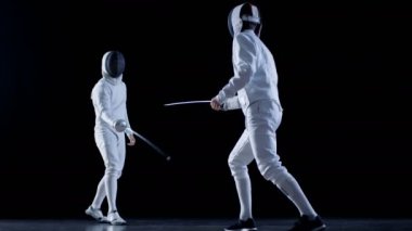 İki profesyonel tam donanımlı eskrimcilerin ustalıkla folyo ile mücadele. Onlar saldırı, savunma, sıçrama, itme ve saldır. Atış yavaş hareket ve siyah arka plan izole. 