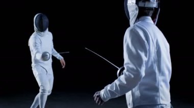 İki profesyonel tam donanımlı eskrimcilerin ustalıkla folyo ile mücadele. Onlar saldırı, savunma, sıçrama, itme ve saldır. Atış yavaş hareket ve siyah arka plan izole. 