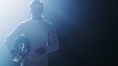 Yakışıklı genç eskrimci Spotlight koyar bir maç için hazır koruyucu maske asansörleri folyo ateşe yürür. Siyah arka plan üzerine izole atış.