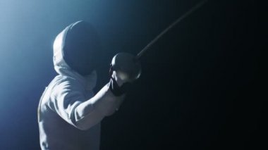 Yetenekli Fencer trenler bir folyo ile tam donanımlıdır. Karanlık etrafında onu ile bir spot ışığı var. O uygulamaları saldırı, savunma, sıçrama, itme ve saldır. Siyah arka plan üzerine izole atış.