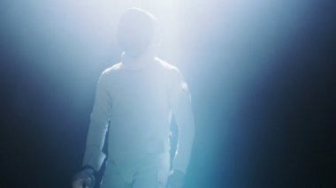 Tam donanımlı Fencer Spotlight koyar asansörleri folyo kılıç bir maç için hazır yürür. Karanlık etrafında onu ise sahne ışıkları altında duruyor. Siyah arka plan üzerine izole atış.