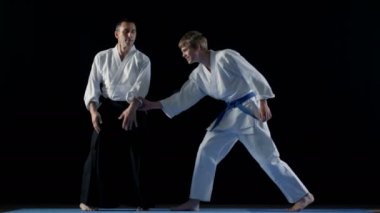 Dövüş sanatları ustası Hakamas giyen genç öğrenci Aikido tekniği öğretir. Siyah arka plan üzerine ve yavaş hareket izole atış. 