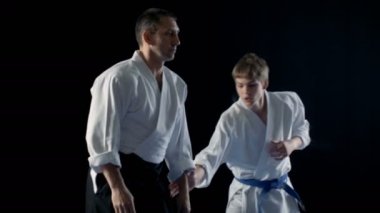 Dövüş sanatları ustası geleneksel samuray Hakamas giyen genç öğrenci Aikido teknik omzunun üzerinden atma öğretir. Siyah arka plan üzerine ve yavaş hareket izole atış. 