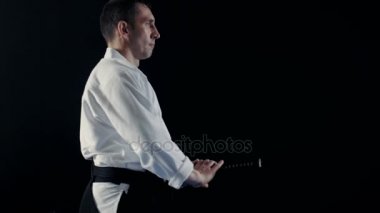 Yan görünümü Aikido Ana giyen geleneksel samuray Hakama giysiler alır onun Japon kılıç kılıç kını ve hali ile o. Onu o spot karanlık çevreler. Siyah arka plan üzerine izole atış.