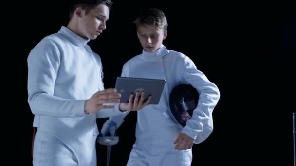 Two Young Fully Equipped Fencers Use Tablet Computer To Learn More About Strategy, Attack and Defense in Fencing. Shot Isolated on Black Background. — Stock Video