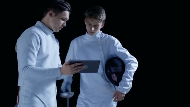 Due giovani schermidori completamente attrezzati utilizzano il computer tablet per saperne di più su strategia, attacco e difesa nella scherma. Girato isolato su sfondo nero . — Video Stock