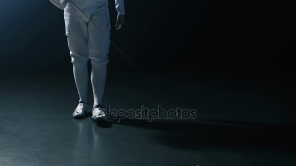 Le beau jeune escrimeur entre en scène met en vedette des ascenseurs de masque de protection pour faire lever l'épée en forme pour un match. Tir isolé sur fond noir . — Video