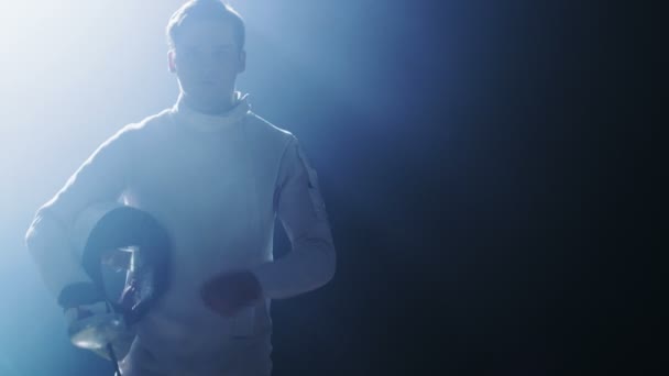 Knappe jonge Fencer loopt in de Spotlight zet op beschermend masker liften folie zwaard in gereedheid voor een wedstrijd. Schot geïsoleerd op zwarte achtergrond. — Stockvideo