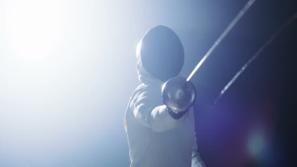 Volledig uitgeruste geschoolde Fencer treinen met een folie. Hij is in een schijnwerper met duisternis rond hem en alleen zwaard van de Partner is zichtbaar. Hij praktijken aanval, verdediging, sprong, Thrust en Lunge. Schot geïsoleerd op zwarte achtergrond. — Stockvideo