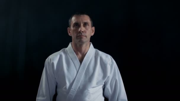 Portrét Shot Aikido Master nošení Hakama tradiční samurajské oblečení procházky na fotoaparát a luky v respektu. On je v okolí Darkness Spotlight on. Shot izolované na černém pozadí. — Stock video